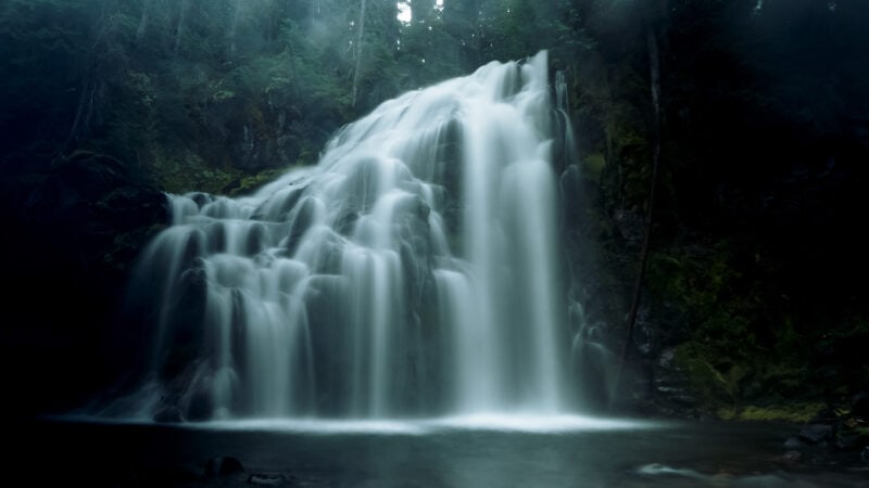 Cascading waterfalls cast  a haze over a dimly lit rocky outcropping