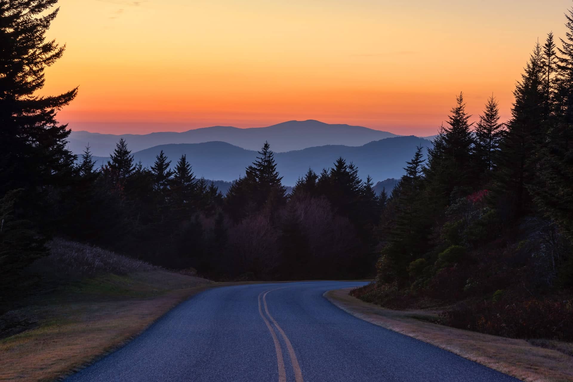 A paved road leads into the Blue Ridge Mountains at sunset
