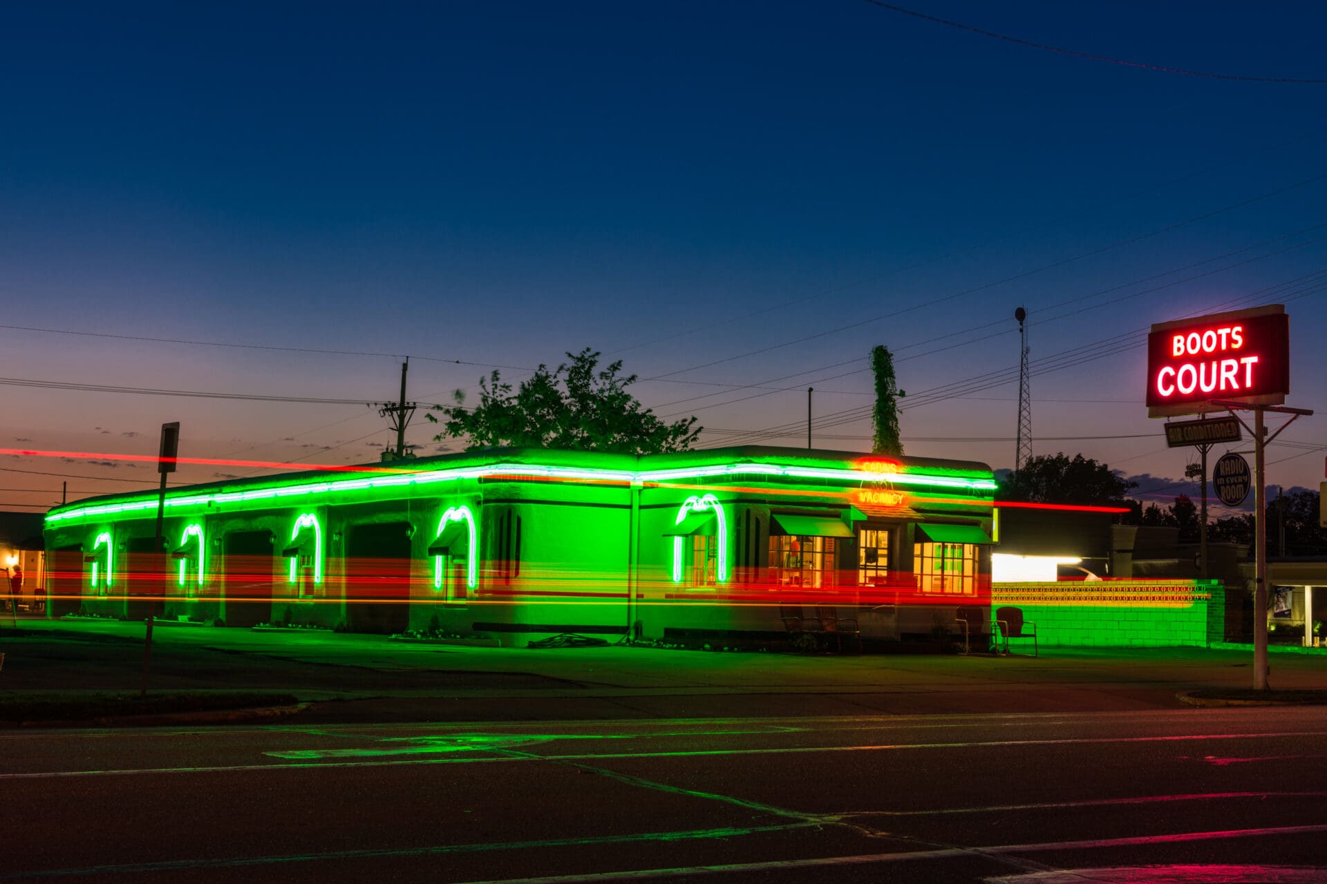 A long exposure photo of Boots Court, a classic Route 66 motel at night with streaks of red and green neon