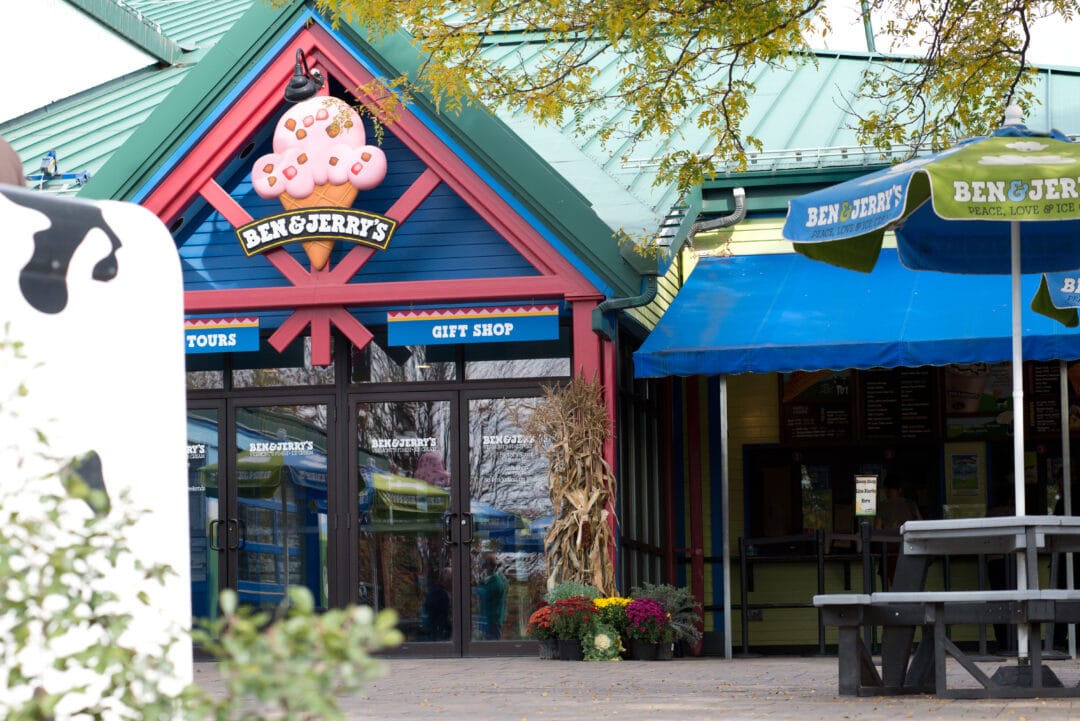 the outside of a ben and jerry's shop with picnic tables and a gift shop sign