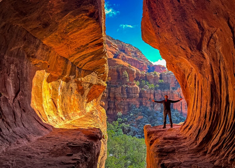A man stands with arms outstretched as he's surrounded by unique red rock formations