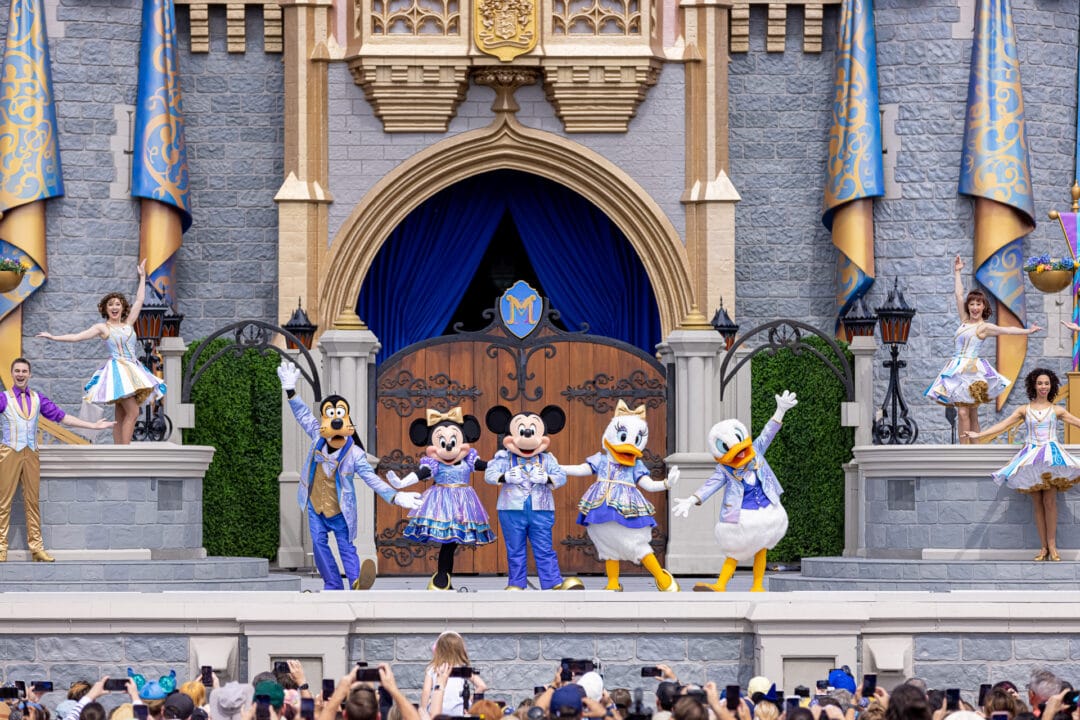 Goofy, Minnie, Mickey, Daisy, and Donald Duck stand in front of Cinderella Castle