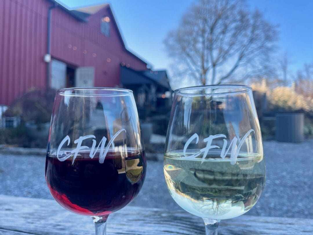 Two wine glasses etched with "CFW" sit in front of a red brick building