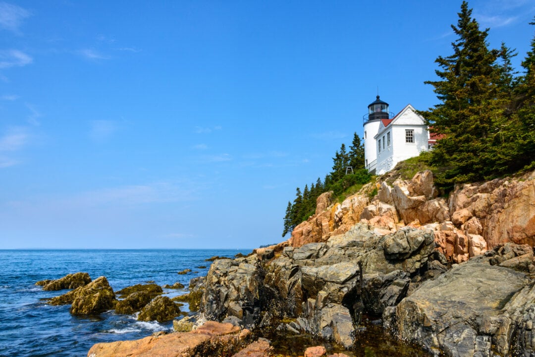 a white lighthouse sits on a rock outcropping above the shore