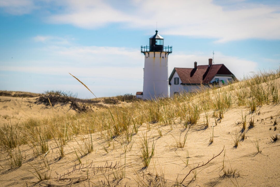 a white lighthouse sits among sandy dunes under a blue sky