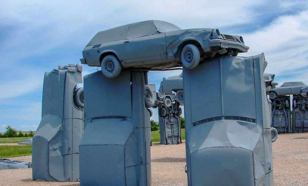 A car sculpture featuring a painted car perched on top of two other cars coming out of the ground