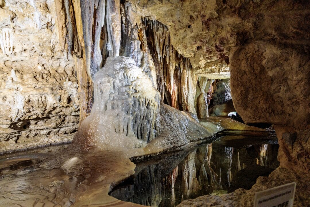 Interior of a cave with long jagged rocks hanging down and a small pool of water
