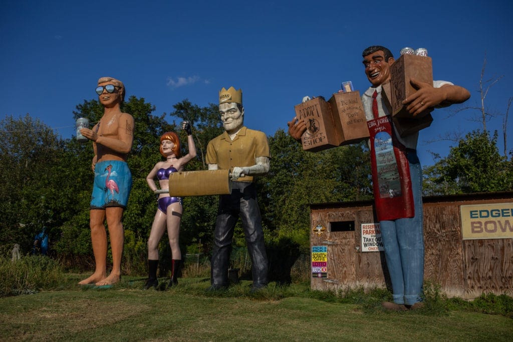 Larger-than-life statues of people and company mascots stand in a field in West Virginia