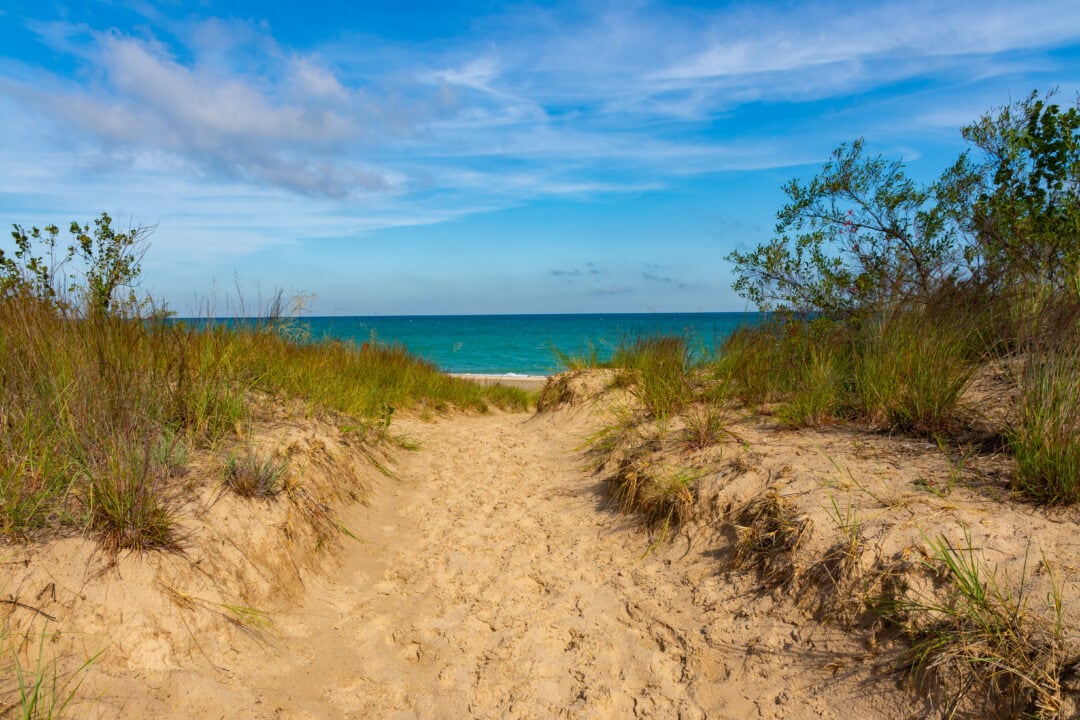 Sandy path through the dunes with a blue Lake Michigan in the background against clear skies