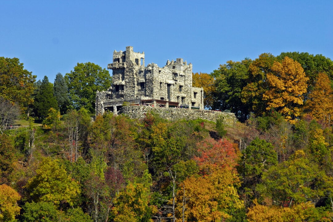a stone castle rises out of colorful fall foliage against a clear blue sky