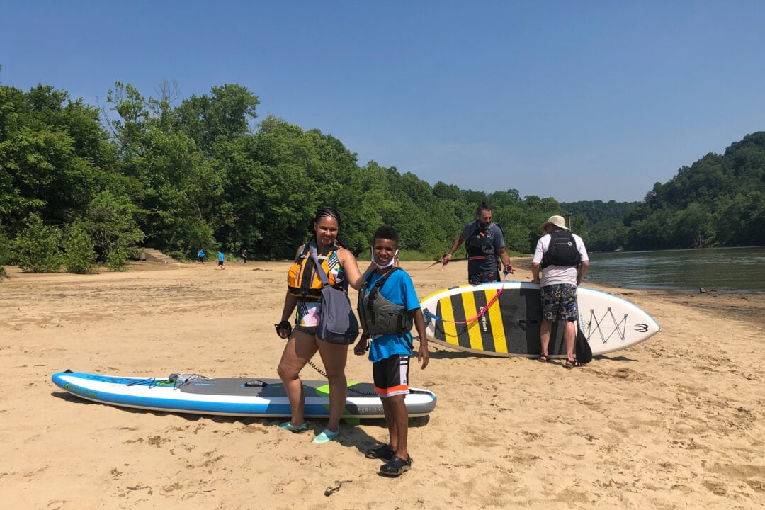 Adults and children take a break from stand up paddleboarding to pose for a photo.