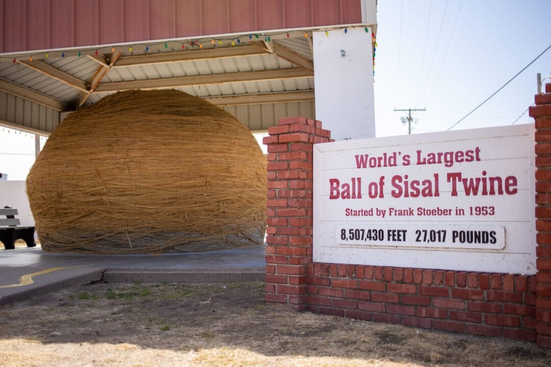 Massive ball of twine sitting under an awning with a sign next to it stating it's the World's Largest Ball of Sisal Twine