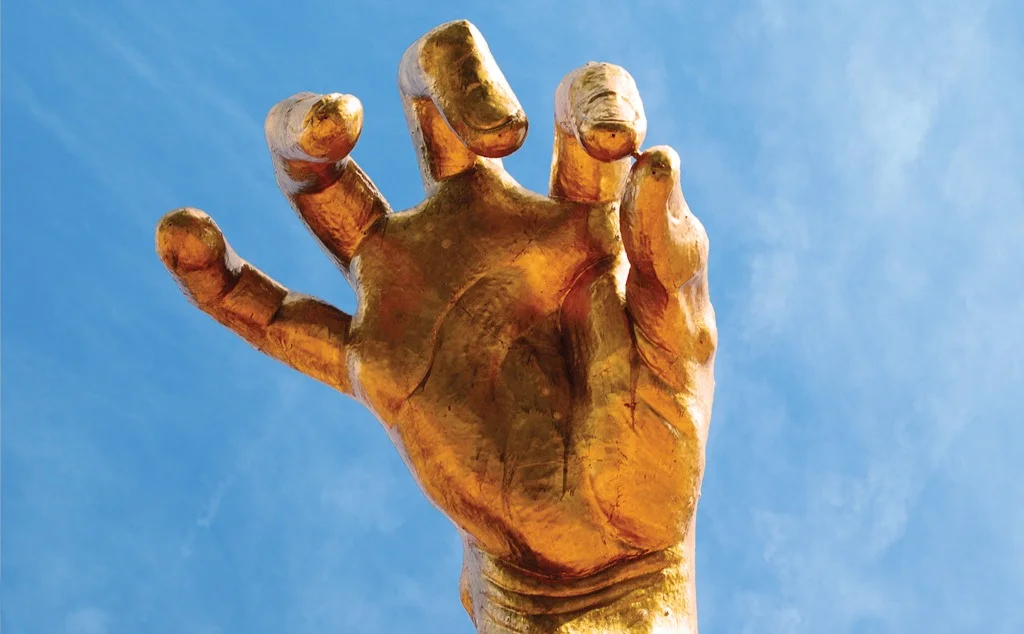 a large golden hand sculpture against a blue sky