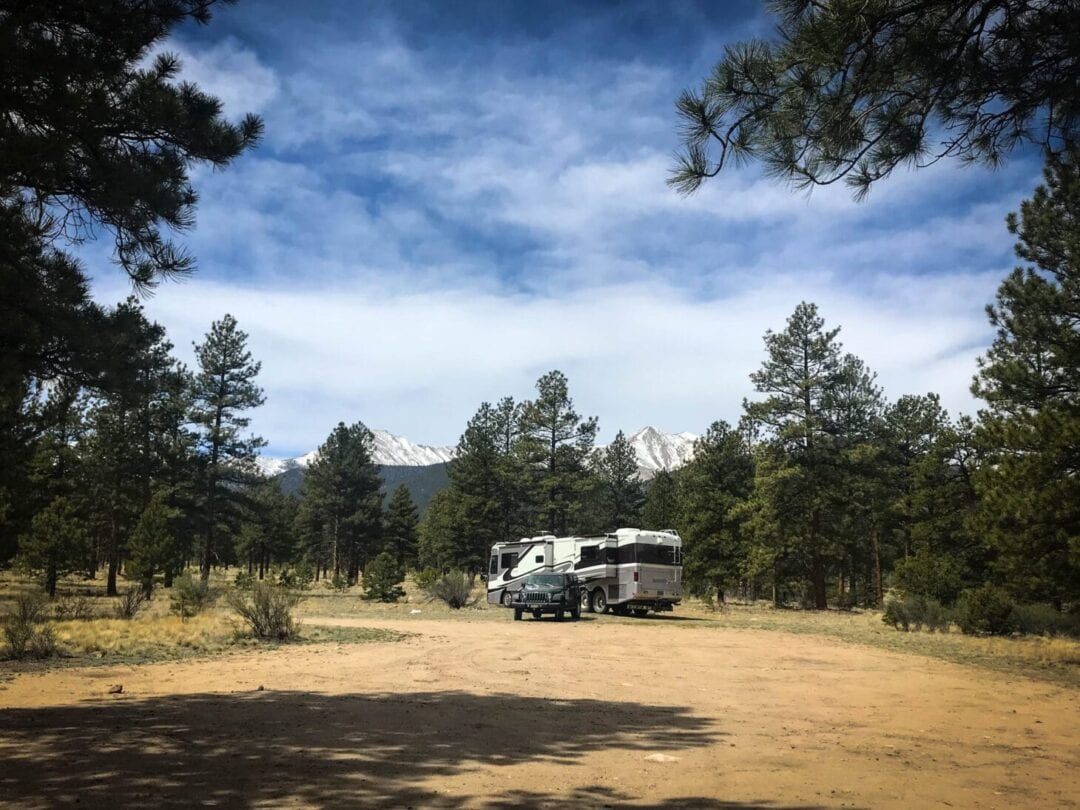 Large RV and towed vehicle parked in dry camping location with snow-capped mountains in distance