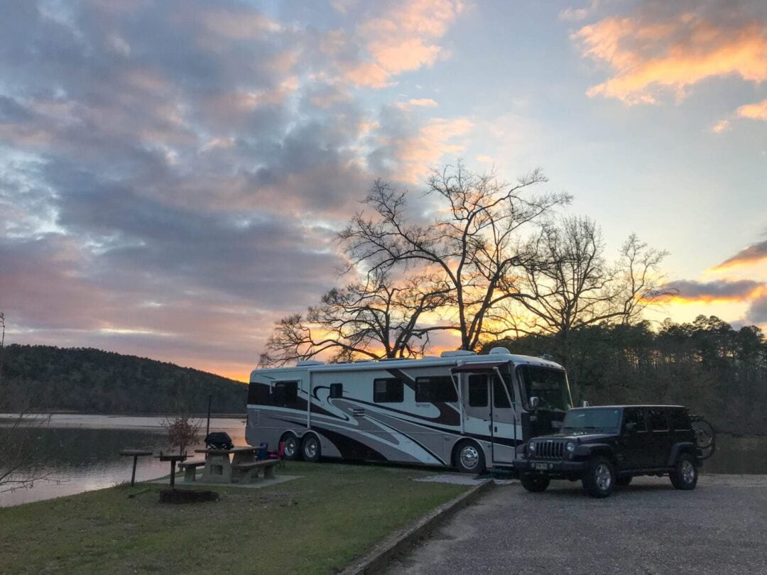 Large RV parked at waterfront campsite with picnic table as sun sets