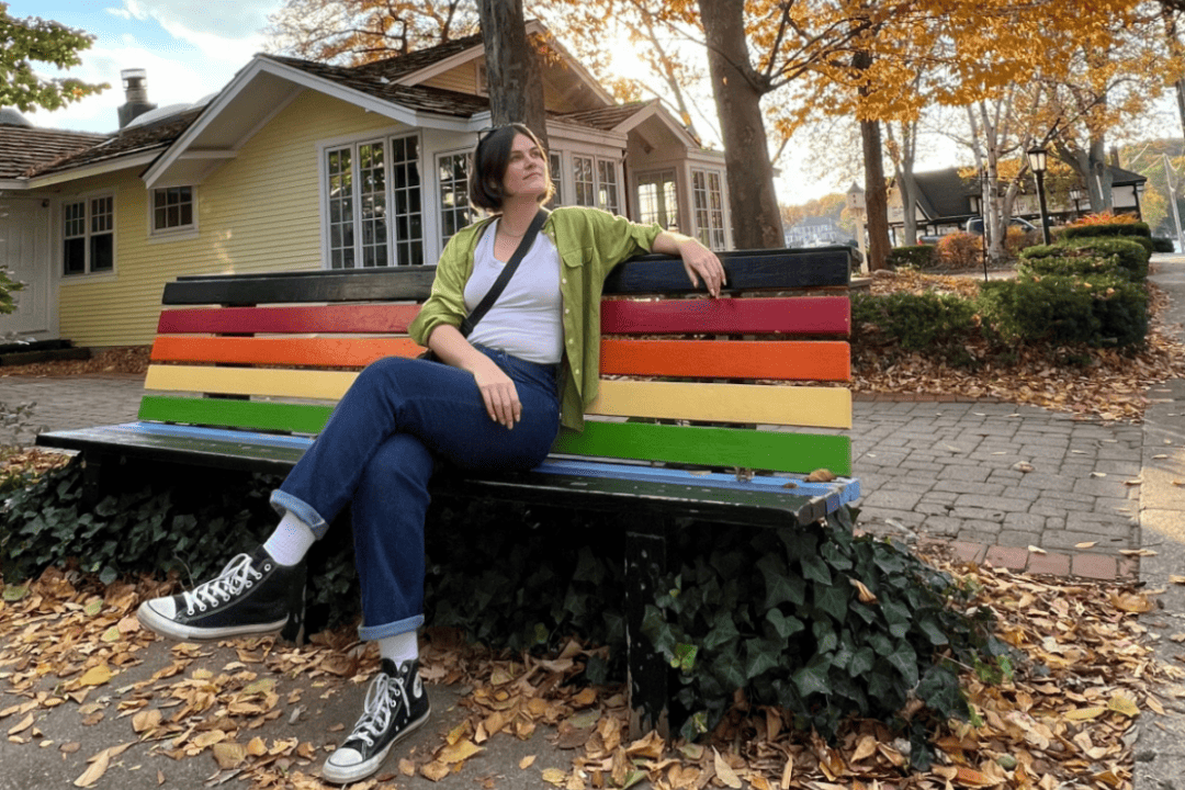 Courtney Vondran sits on a rainbow colored bench surrounded by fall leaves