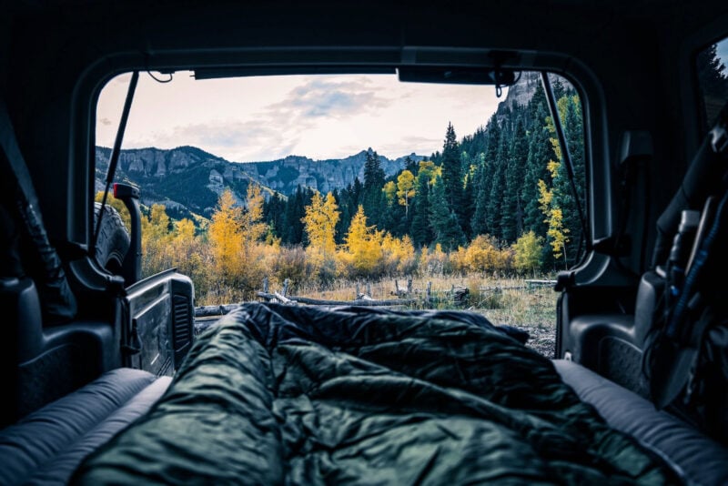 The back hatch of a car is open to reveal a sleeping spot with mountain views