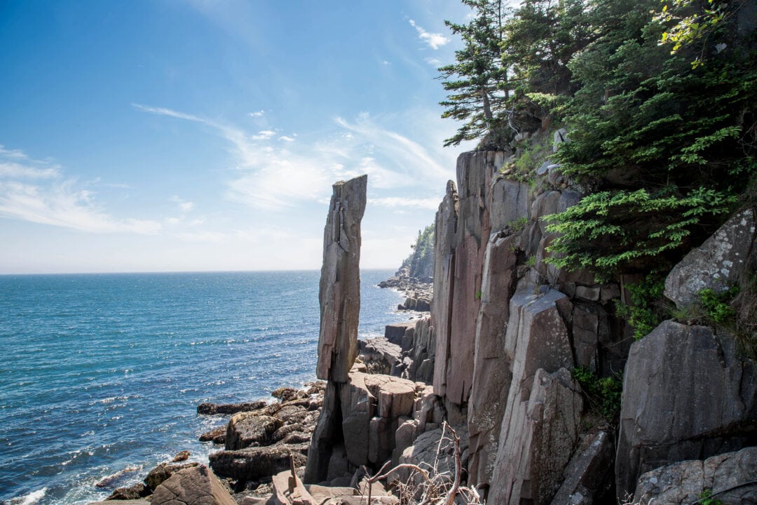 A tall rock formation balances atop another rock next to the ocean
