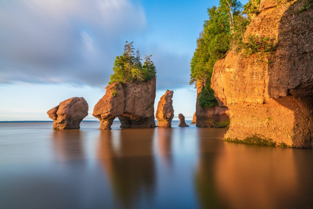 A stunning group of rock formations stand in the water, as seen from land