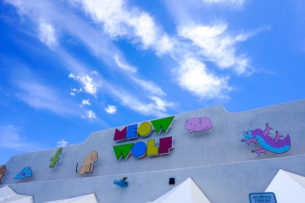 A multi-color sign for Meow Wolf stands on the building's exterior