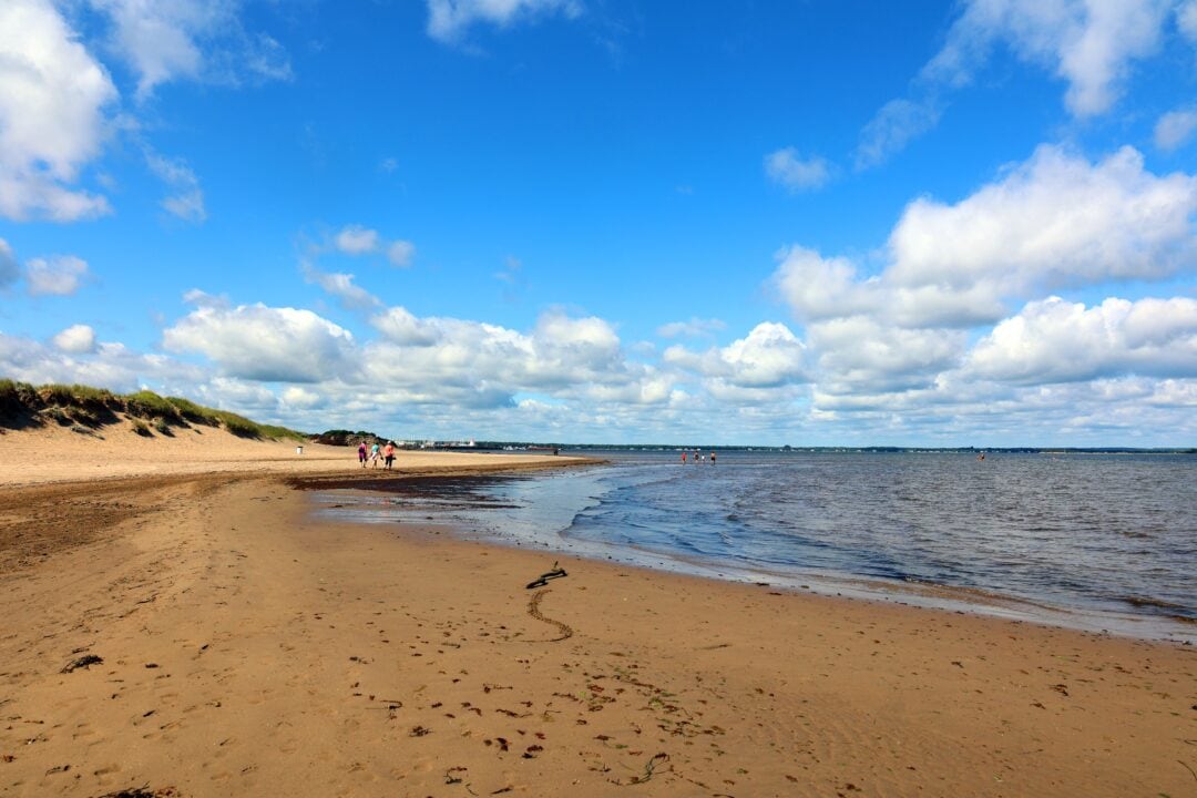 A sandy beach with a low tide and people walking in the background