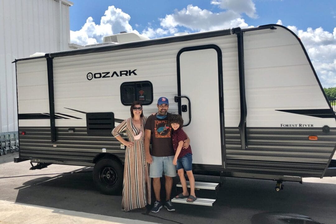 Family of three stands outside a newly purchased travel trailer