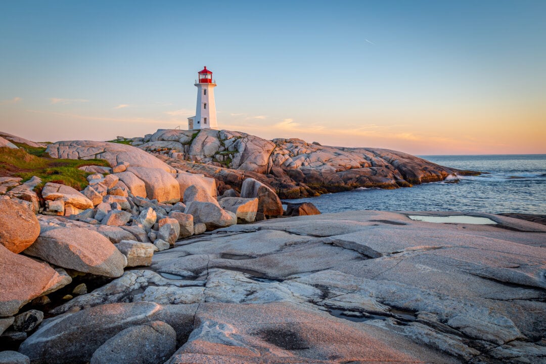 A lighthouse stands on beachside cliffs at sunset