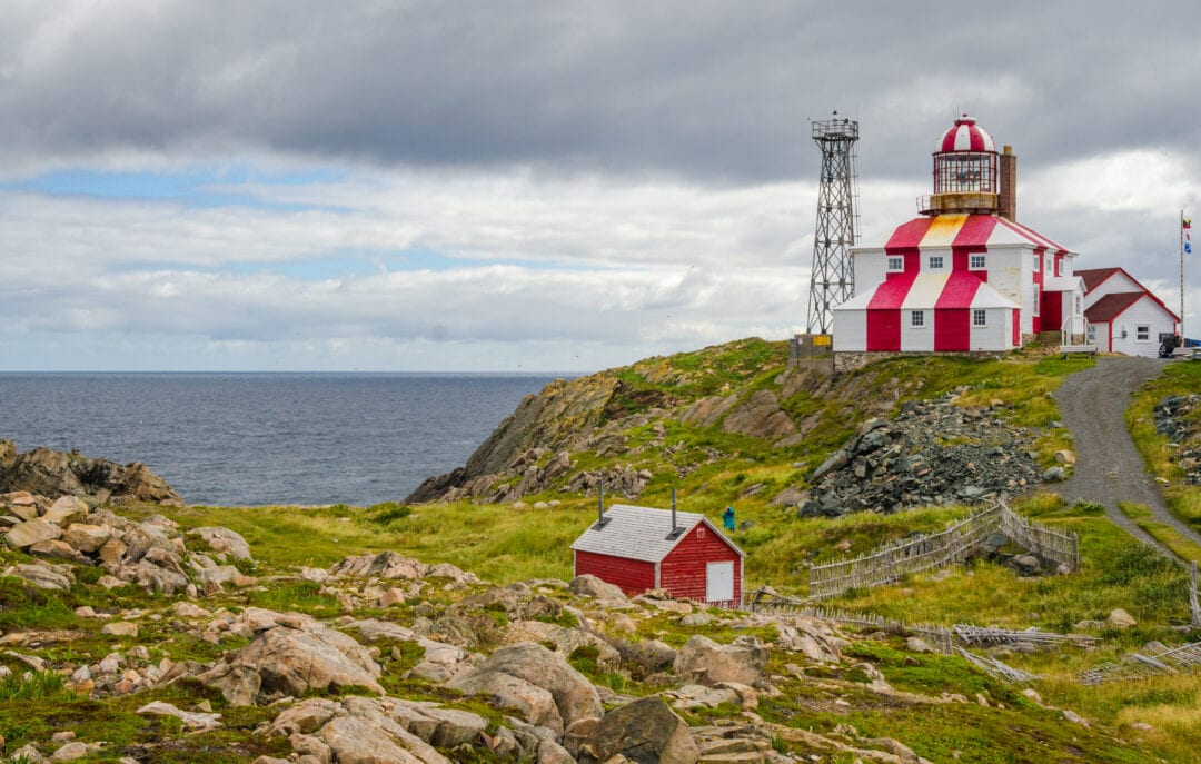 A striking red and white striped lighthouse sits atop a grassy cliff