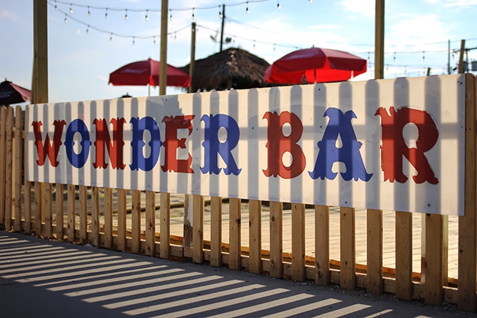 a wooden fence at the beach with a sign for the Wonder Bar
