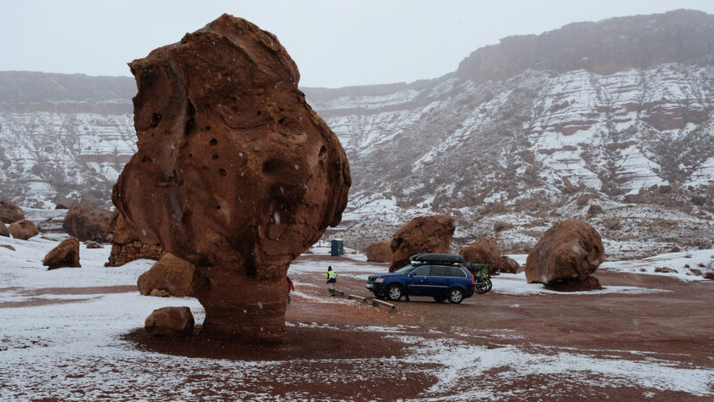 A blue car sits amid towering boulders covered in snow