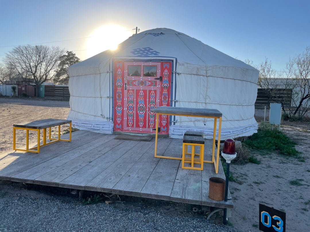 A white yurt with a red door and deck sits in Marfa, Texas