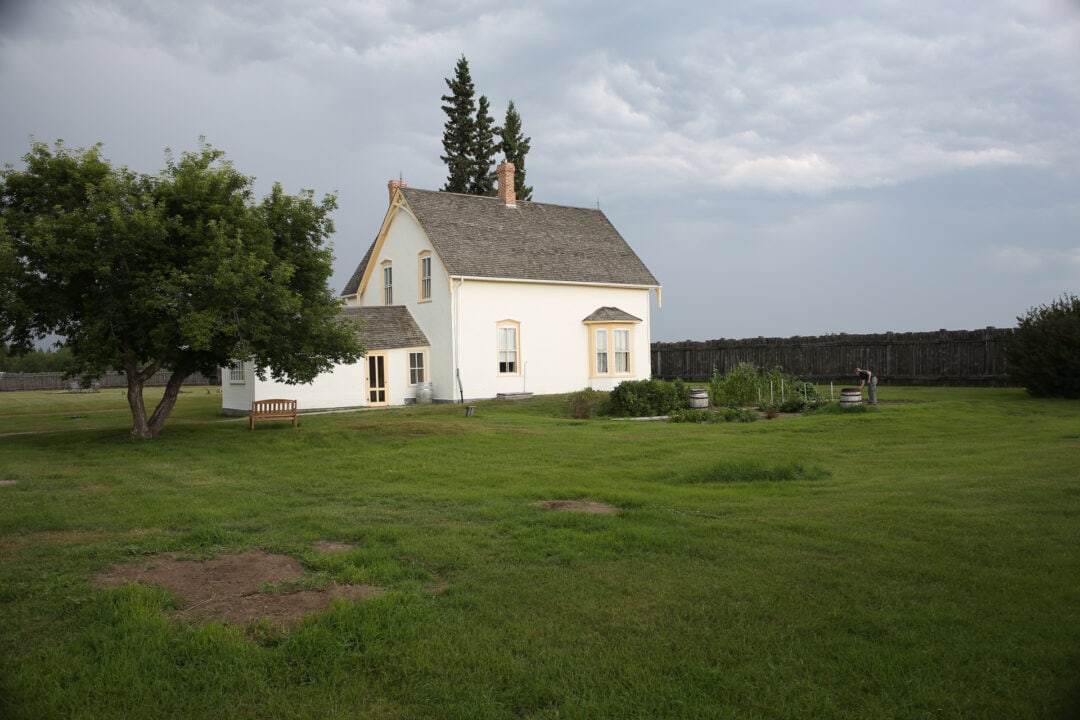 White building with person tending to garden at Fort Battleford in Canada
