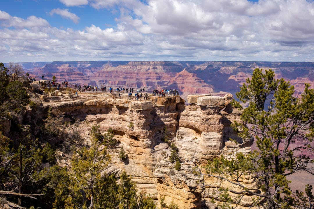 people stand on a rock outcropping overlooking the grand canyon
