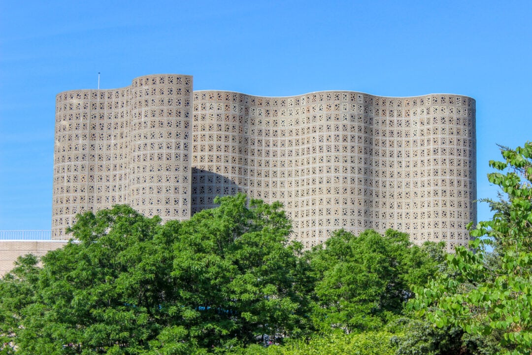 an undulating concrete building set against a clear blue sky with green trees in front