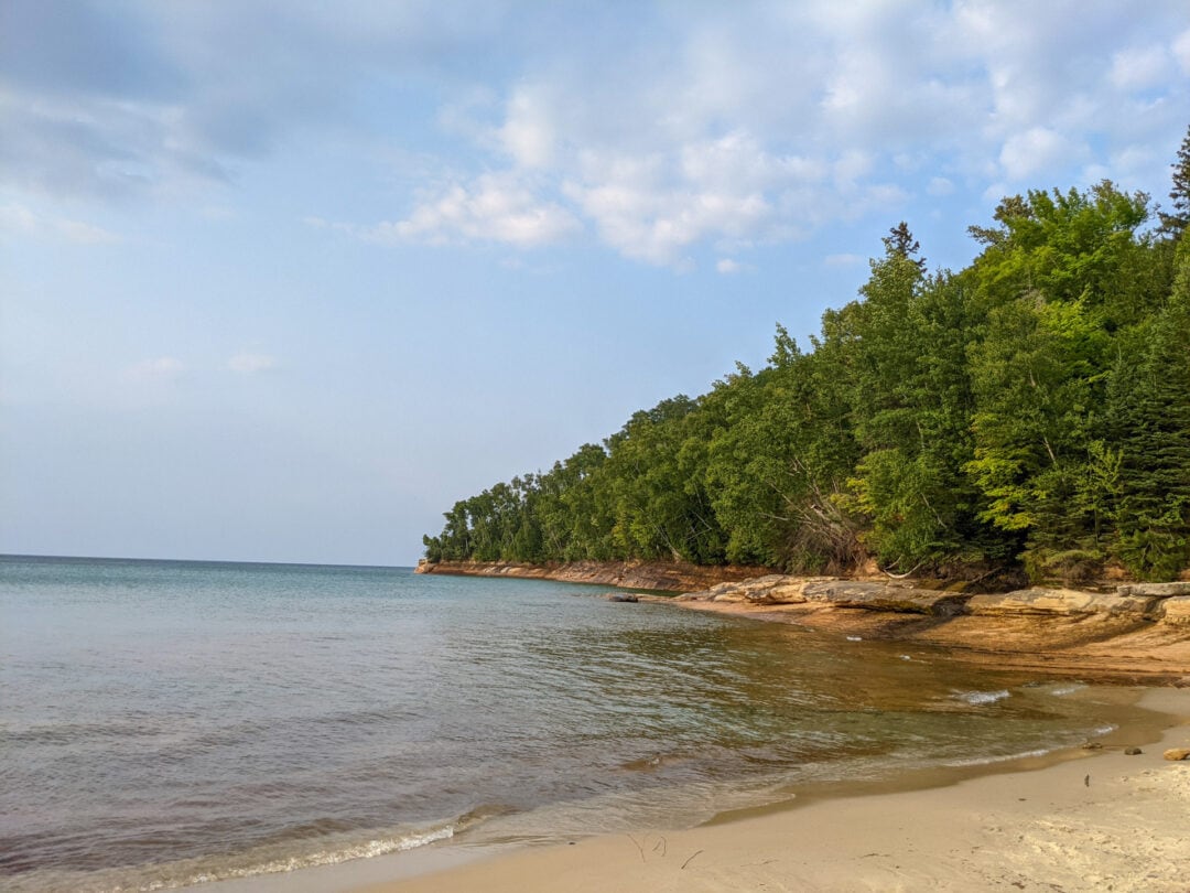 A sandy beach and rocky lake coastline with trees