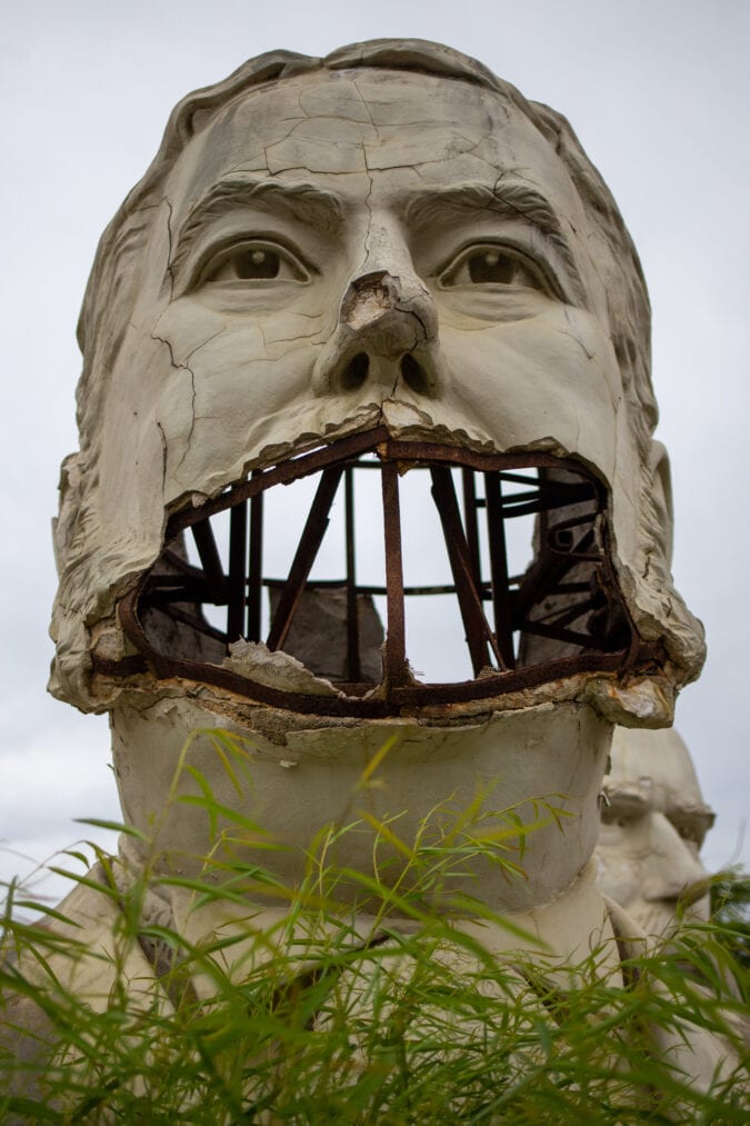 a large bust of chester a arthur crumbling in a field and missing most of its mouth