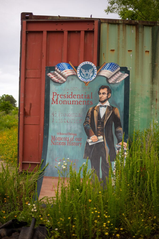 a handpainted sign of abraham lincoln is leaning up against a shipping container in a grassy field