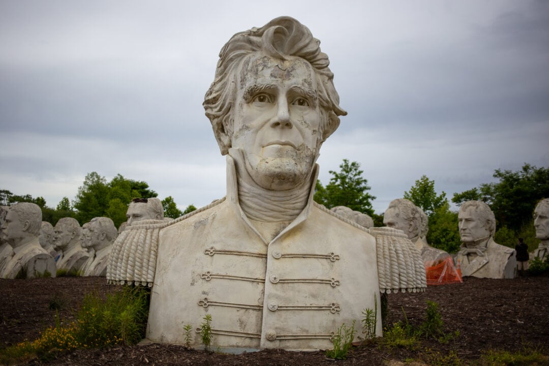 a large white crumbling bust of andrew jackson in a field with other similar presidential busts