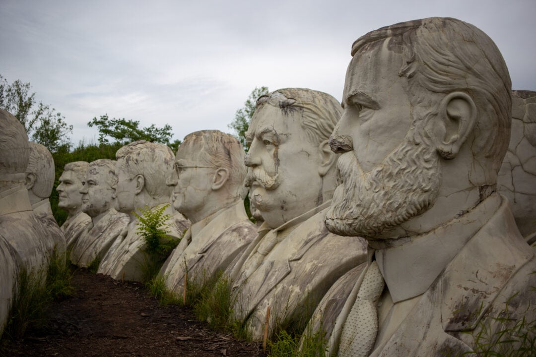 several large busts of u.s. presidents crumbling in a field under a grey sky