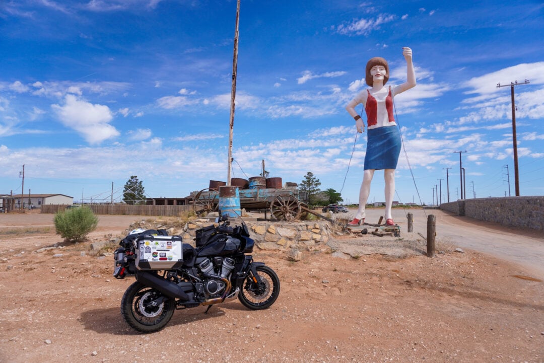 A motorcycle parked next to a tall fiberglass woman wearing a blue skirt and holding up one hand
