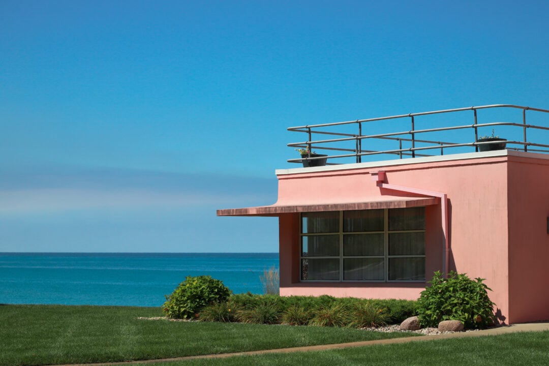 a pink modern house overlooks a blue lake under a clear blue sky