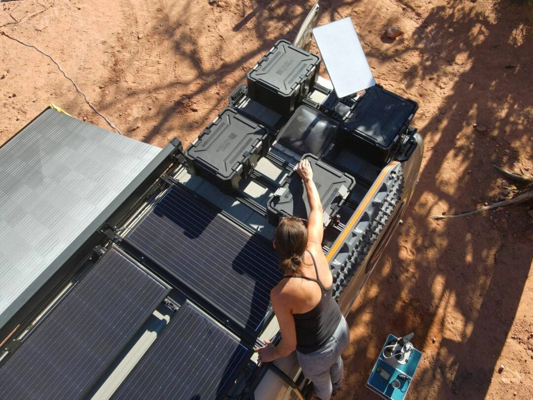 A person adjusts electric components on top of an RV.