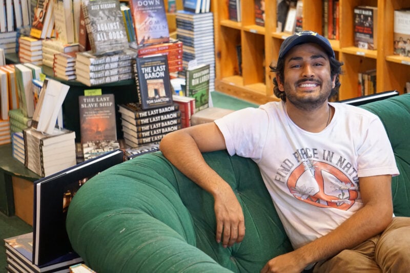Tushar Varma sits on a green velvet couch surrounded by books