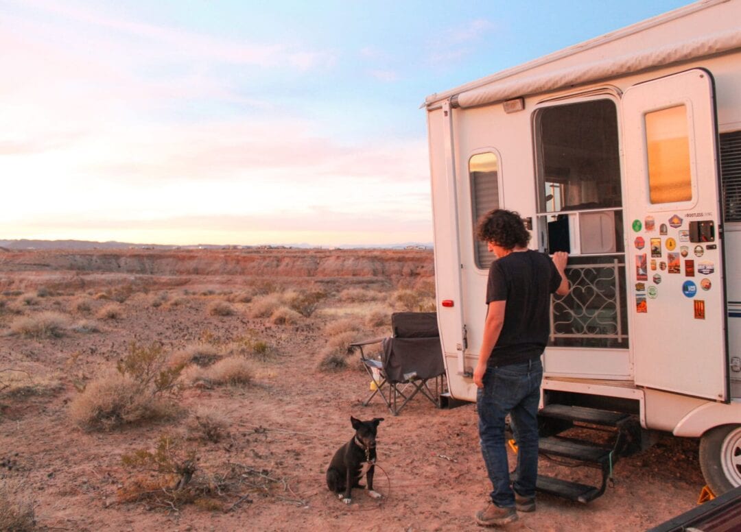 Man entering RV in desert setting observing dog