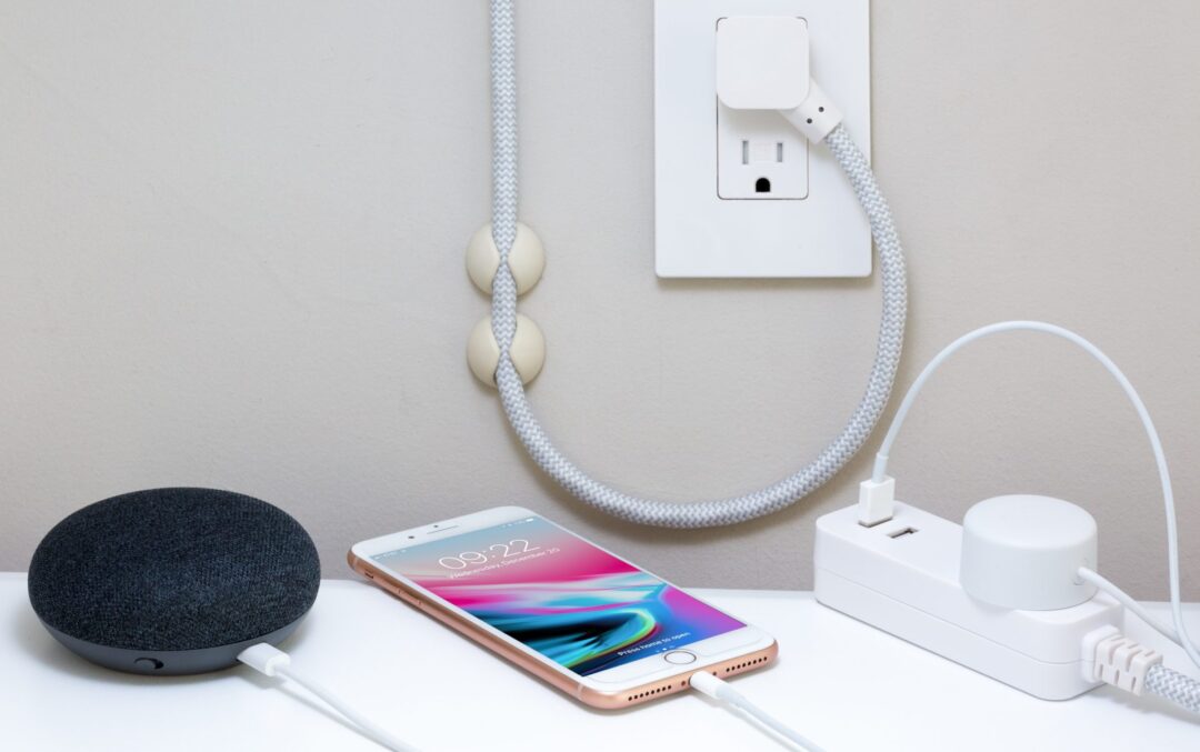 a desk with an iphone, extension cord and speaker plugged into an outlet