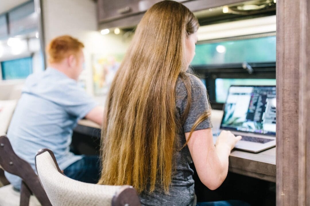 two people sit at a desk working on computers in an rv