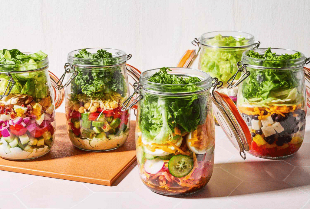 Jar salads with dressing, greens, and vegetables.